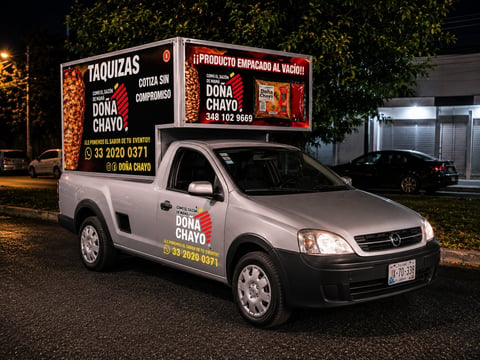 White Chevrolet pickup truck with advertising sign on top for Dona Chayo restaurant at night