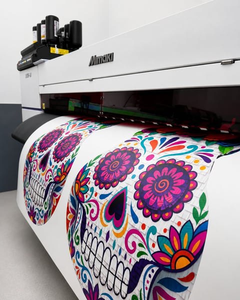 Large format inkjet printer displaying colorful skull and flower design on white fabric roll